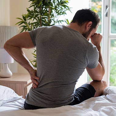 Man sitting on bed suffering from sciatica prior to chiropractic treatment