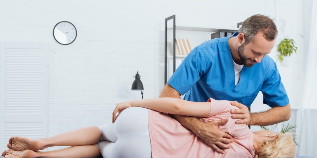 smiling-chiropractor-massaging-back-of-patient-that-lying-on-massage-table-in-hospital.jpg